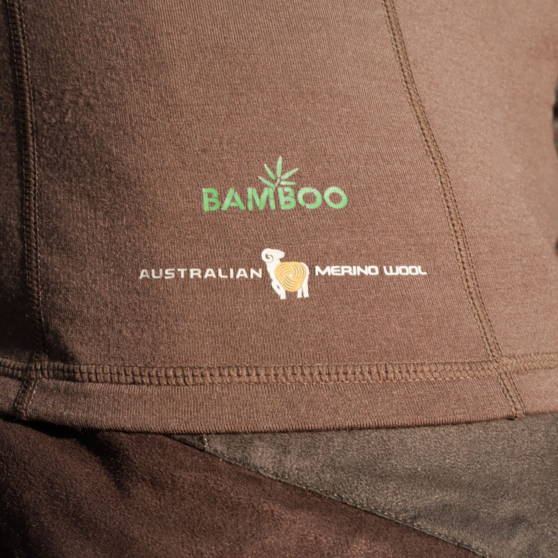 Close-up of Hillmans brown 2BL Merino Wool Base Layer-Hunting Long Sleeve Thermal T-shirt, featuring BAMBOO-MERINO TECHNOLOGY and AUSTRALIAN MERINO WOOL with a sheep logo. Green and white text highlights the materials advanced thermal regulation properties.